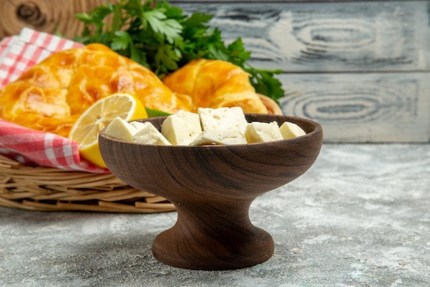 Side view from afar pies and lemon plate of cheese and pies herbs lemon and lime and tablecloth in the basket on the wooden background