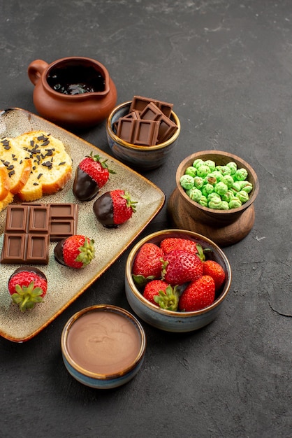 Side view from afar strawberry cake chocolate bowls of chocolate strawberries green candies and chocolate cream appetizing cake and strawberries on the left side of the table