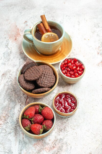 Side view from afar tea with lemon chocolate cookies a cup of tea bowls of strawberries jam