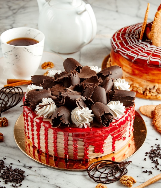 Side view of fruit cake topped with chocolate curl and whipped cream on the table served with tea