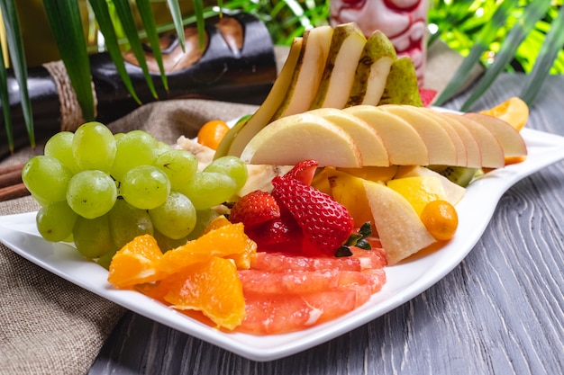 Side view fruit plate orange strawberry banana kiwi pear grapes and cherry plum