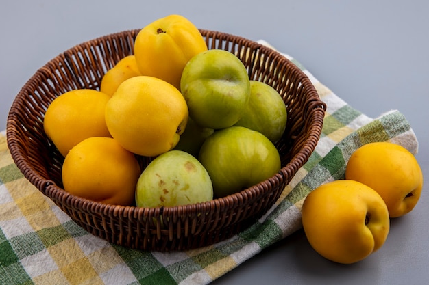 Side view of fruits as green pluots and nectacots in basket on plaid cloth and on gray background