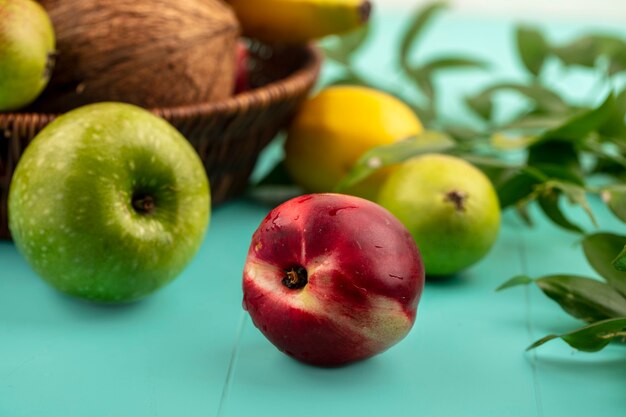 Side view of fruits as peach apple pear lemon with basket of coconut banana and leaves on blue background