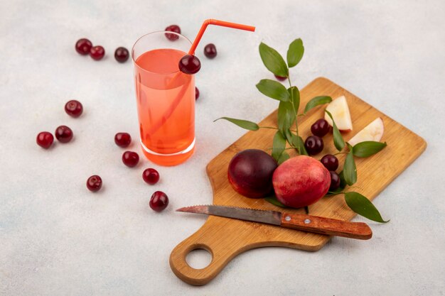 Side view of fruits as peach and cherry with knife on cutting board and cherry juice on white background