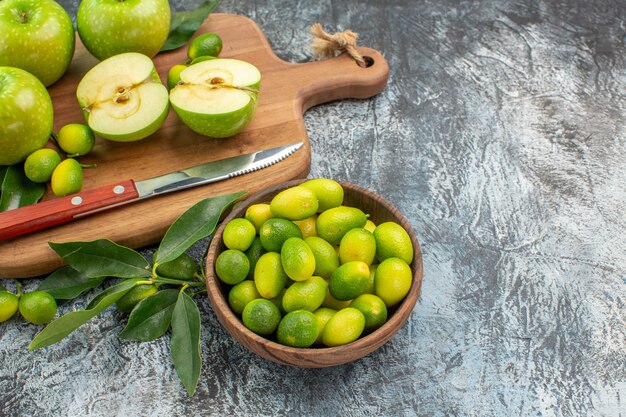 Side view fruits bowl of citrus fruits green apples and knife on the cutting board