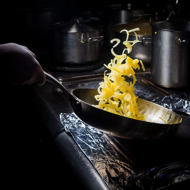 Free photo side view frying onions with pan and human hand in stove