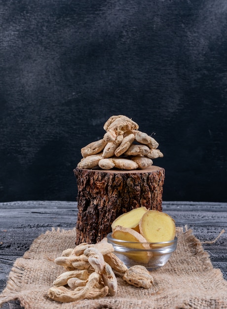 Side view ginger with ginger slices on wood stub, sack cloth and dark wooden background. vertical