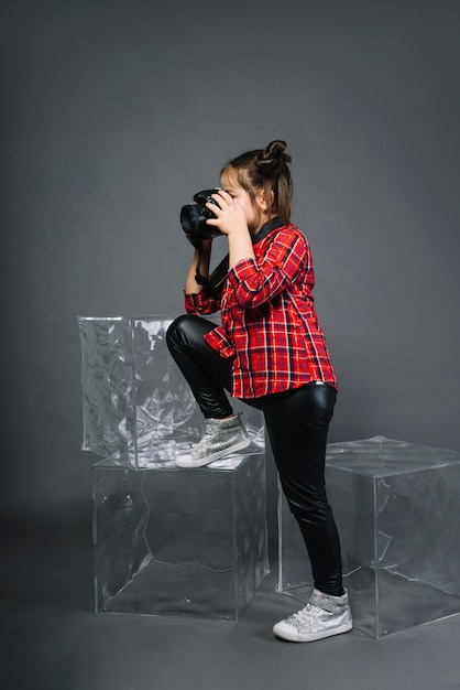 Free photo side view of a girl photographing with camera standing near the blocks