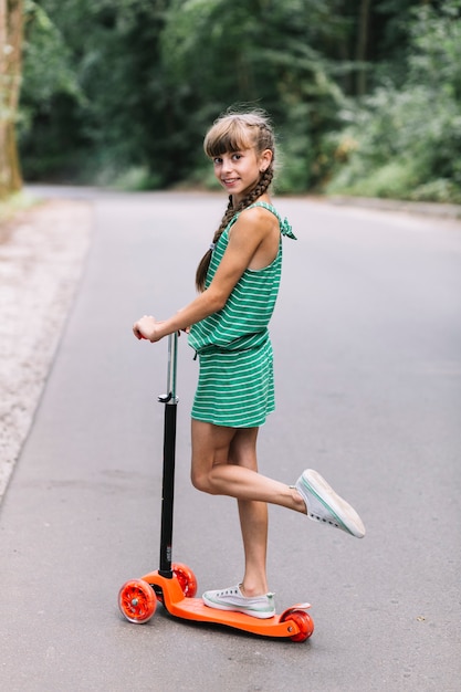 Free photo side view of a girl standing on one leg over the scooter on road