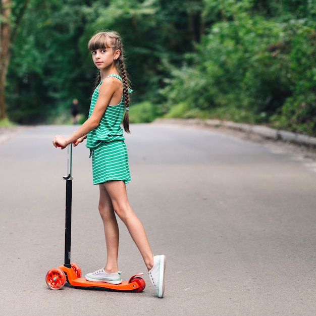 Side view of a girl standing over the scooter on road