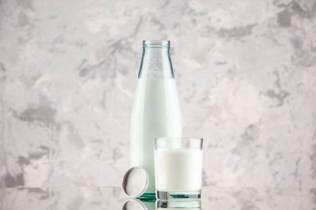 Free photo side view of glass bottle and cup filled with milk cap on pastel colors background with free space