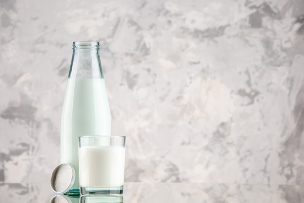 Side view of glass bottle and cup filled with milk cap on the right side on pastel colors background with free space