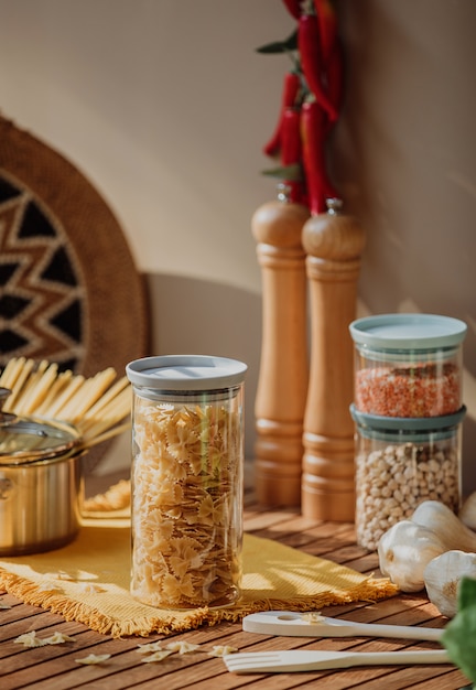 Side view of a glass jar filled with raw farfalle pasta on a wooden table