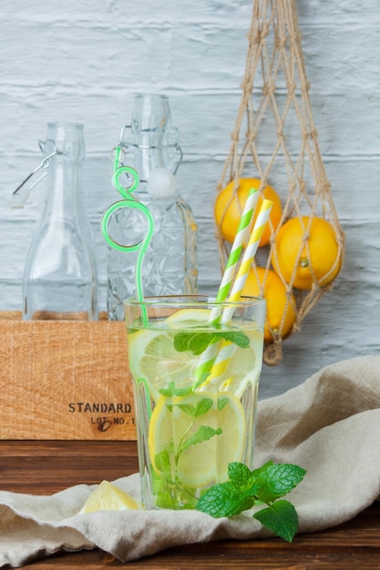 Side view glass of lemon juice with wooden crate and lemons on wooden and white surface. vertical