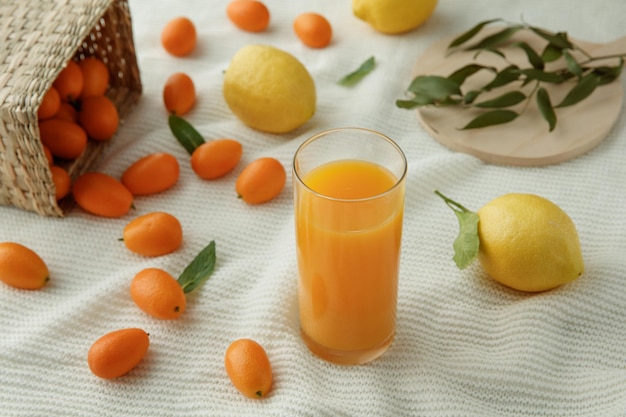 Side view of glass of orange juice with lemons leaves and kumquats spilling out of basket on white cloth background