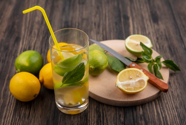 Side view glass of water with lemon  lime and mint slices with yellow straw on wooden background