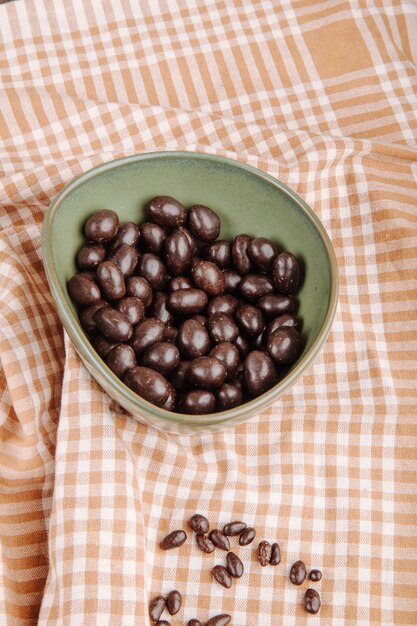 Side view of glazed chocolate nut candy in a bowl on plaid tablecloth