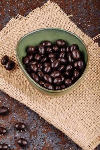 Side view of glazed chocolate nut candy in a bowl on sackcloth on rustic background