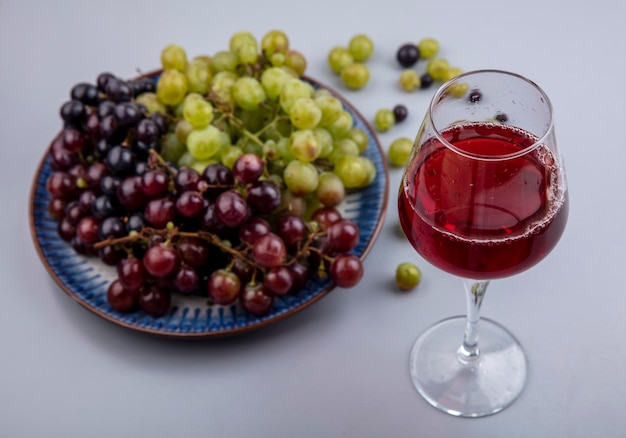 Free photo side view of grape juice in wineglass and grapes in plate and on gray background