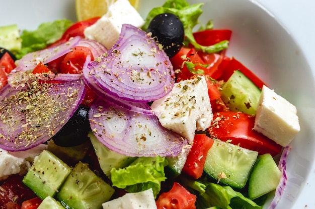 Side view greek salad with white cheese red onion black olive tomato cucumber lettuce oregano and olive oil