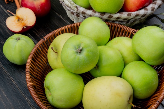 Side view of green apples in basket with whole and cut apples on wooden surface