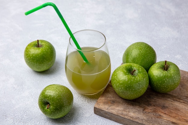 Side view green apples with apple juice in a glass and a green straw on a white background