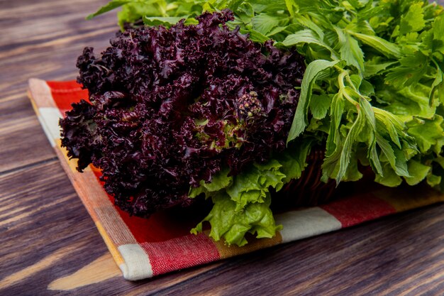 Side view of green vegetables as coriander mint lettuce basil in basket on cloth on wooden table