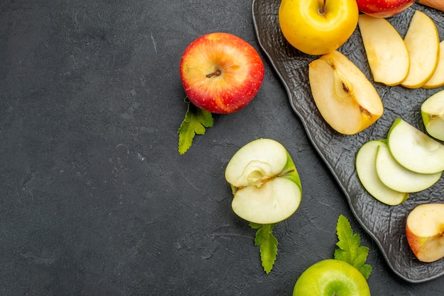 Free photo side view of green yellow and red sliced and whole fresh apples on a black tray and cinnamon limes on a dark table