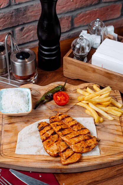 Side view of grilled chicken fillet with french fries on a wooden board