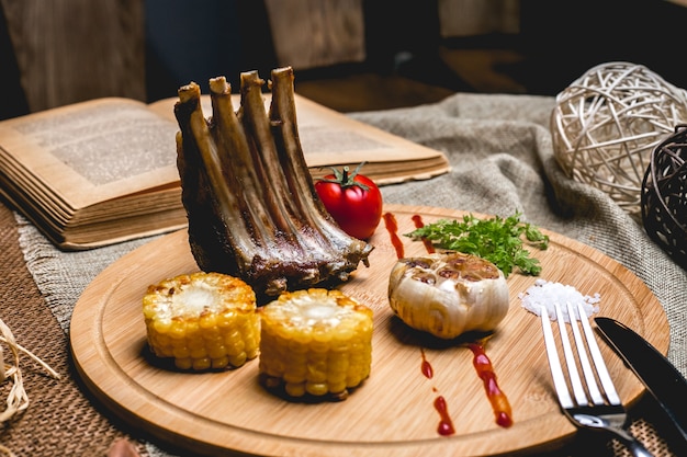 Free photo side view grilled lamb ribs with corn garlic tomato and salt on a board