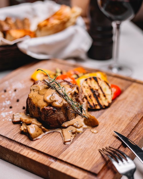 Free Photo side view of grilled meat medalion with sauce and grilled vegetables on a wooden board