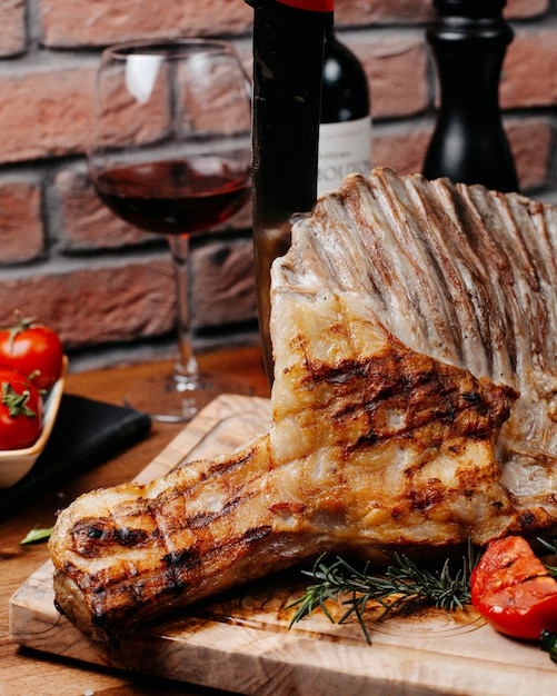 Side view of grilled ribs served with vegetables on wooden board