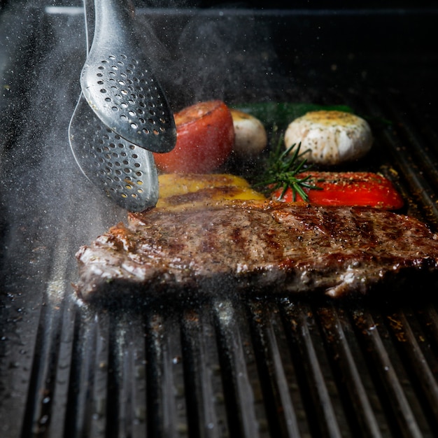 Free Photo side view grilled steak with rosemary and mushrooms and barbecue tongs in barbecue