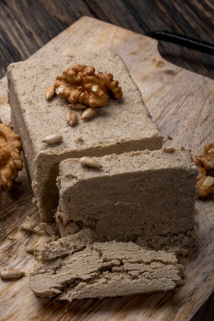 Side view of halva with sunflower seeds and walnuts on a wooden board