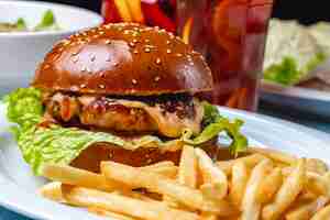 Free photo side view hamburger grilled beef patty with melted cheese sauce lettuce between burger buns and french fries on the table