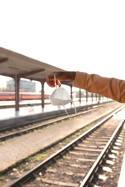 Free photo side view hand holding mask at train station