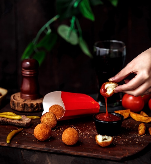 Free Photo side view of a hand putting fried cheese ball into ketchup