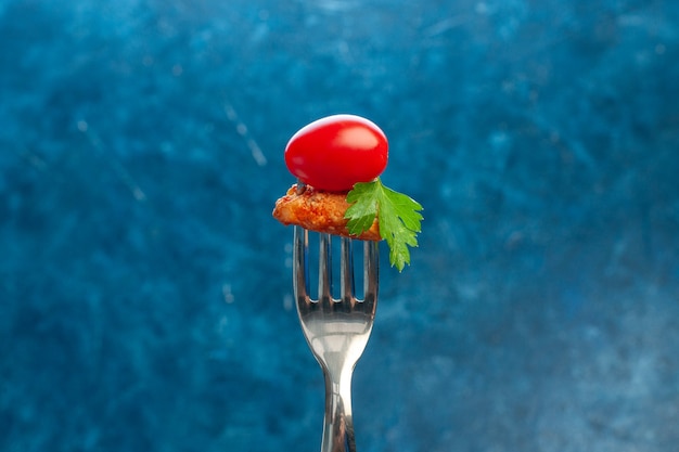 Side view of hand taking a fork tomato and chicken on blue background