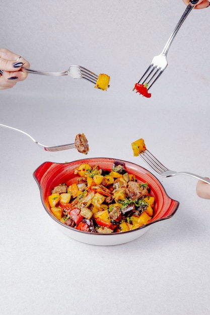 Free Photo side view of hands hold forks over the bowl with stewed meat potatoes and vegetables