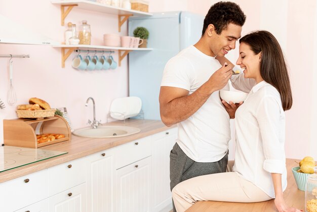 Side view happy couple eating in the kitchen