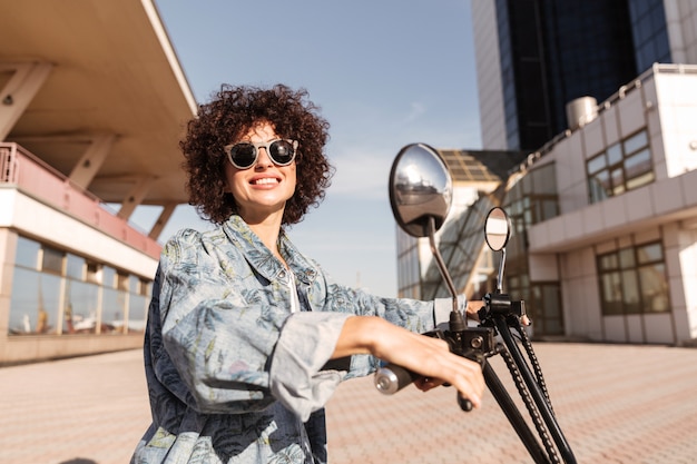 Side view of happy woman in sunglasses posing on motorbike