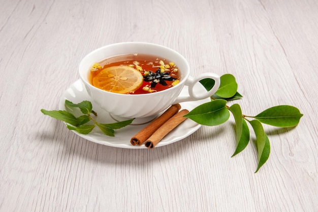 Side view herbal tea a cup of herbal tea with lemon and cinnamon sticks on the saucer and leaves on the white table