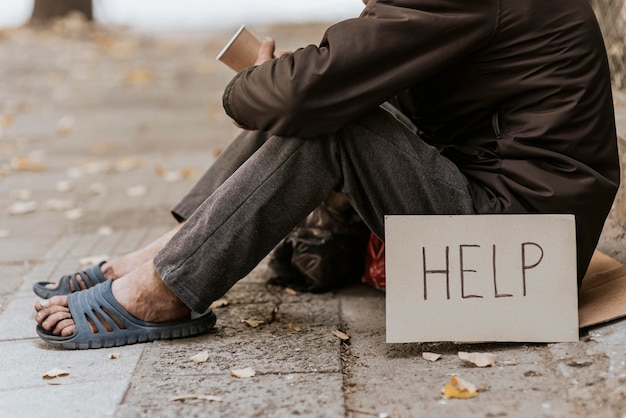 Side view of homeless man on the street with cup and help sign