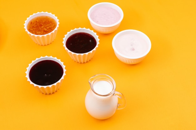 Side view of jam with milk and yogurt on yellow surface horizontal