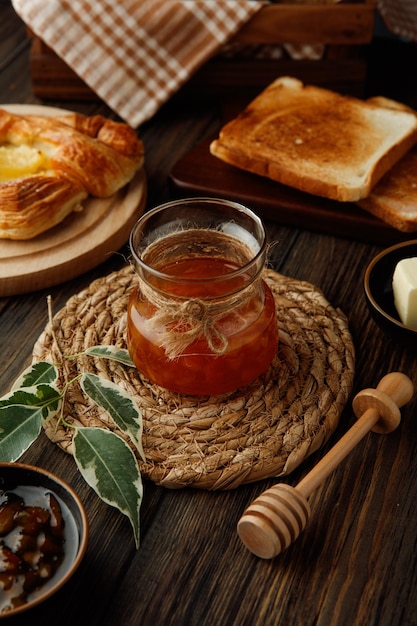 Side view of jar of quince jam on trivet with dried bread slices croissant on wooden background