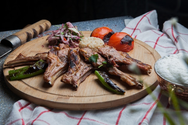 Side view kebab ribs with fried vegetables and chopped onion and knife and ayran in wooden food tray