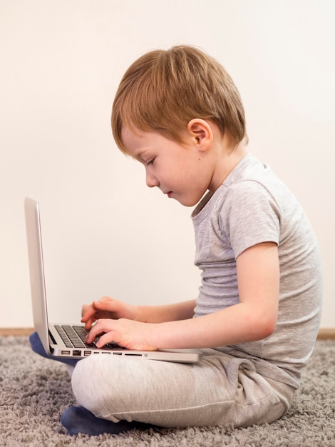 Side view kid playing on the floor with his laptop