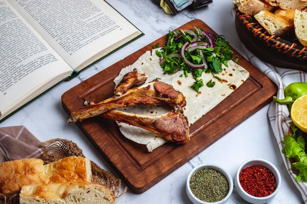 Side view of lamb rib kebab with herbs and onion on a wooden board