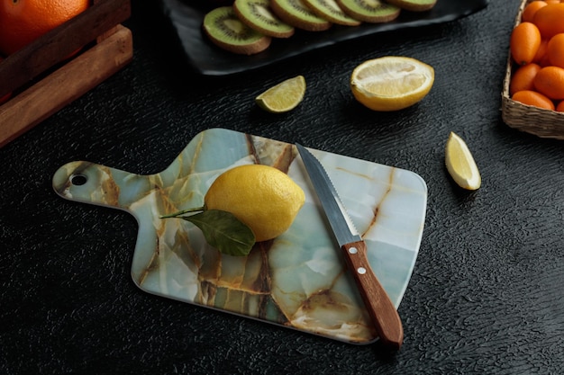 Side view of lemon with knife on cutting board with kiwi slices lime slice cut lemon and whole kumquats on black background