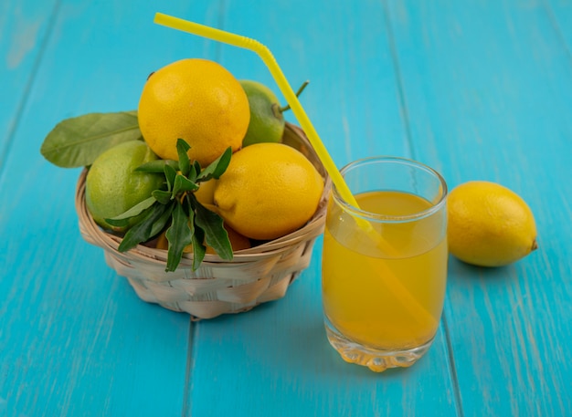 Free Photo side view lemons and limes in a basket and a glass of lemon juice on a turquoise background